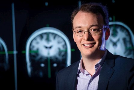 Dr. Jarred Younger, PhD (Professor Associado, Psicologia) que está na frente do grande monitor mostrando imagens de um cérebro de 2014.