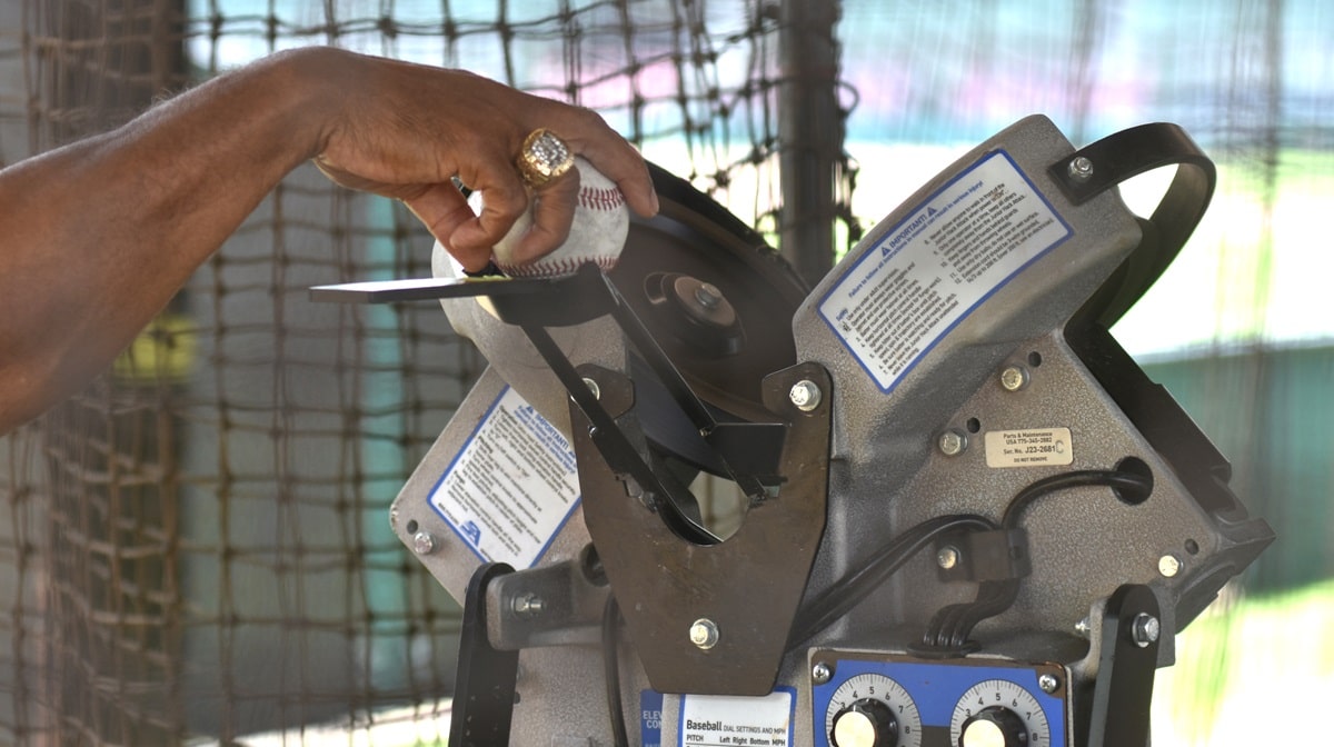 Jerry Manuel puts a baseball into a pitching machine. (Solomon Crenshaw Jr. / Alabama News Center)