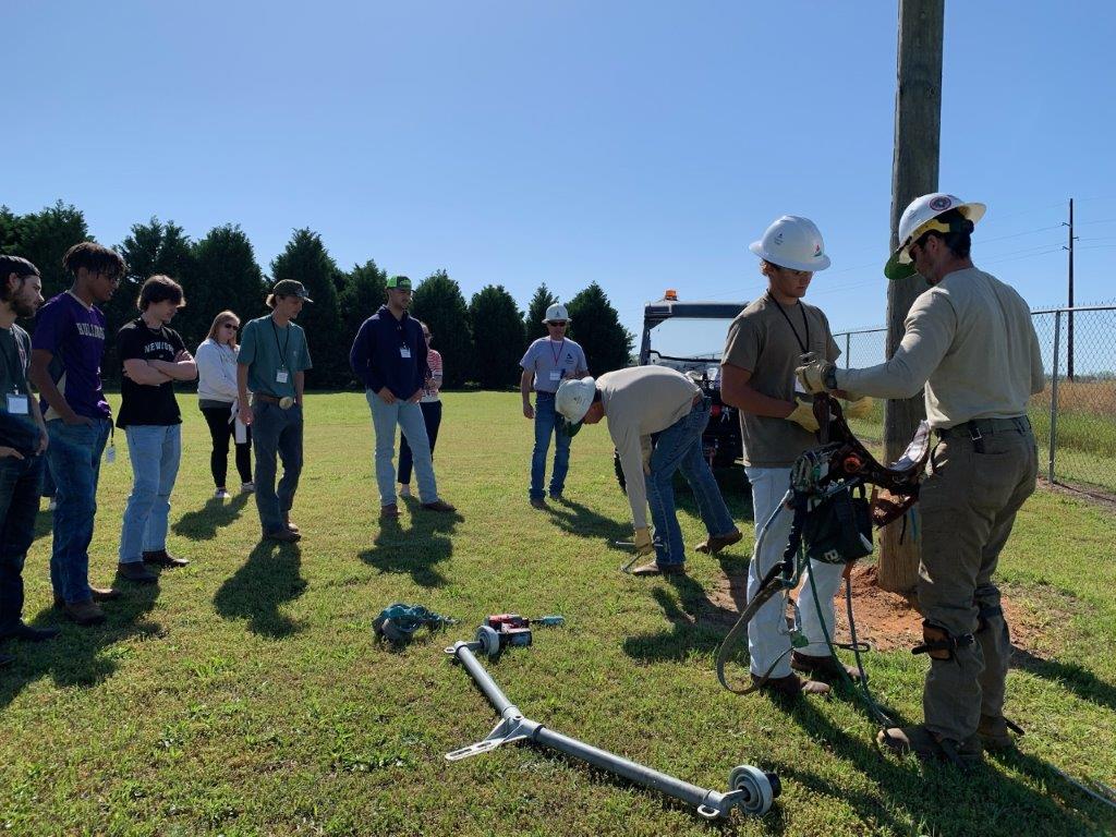 Lineman Drex Roach, far right, shows students how to put on safety harness during a pole-climbing demo at Headland Lineworker Career Day. (Teisha Wallace / Alabama News Center)